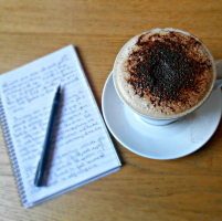 A picture of a notebook with writing in it, a pen, and a cup of coffee