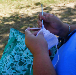 A picture of the hands of a black woman crocheting light colored thread into a
			rectangle.